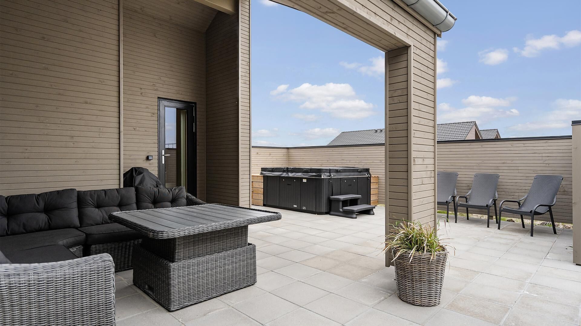 An outdoor patio with a sofa, a table, and chairs, a hot tub, and a potted plant.
