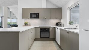 A modern kitchen with a built-in oven, a coffee maker, and a window providing natural light. - VillaVilla 929 - Hvide Sande, Vestjylland (Hvide Sande)