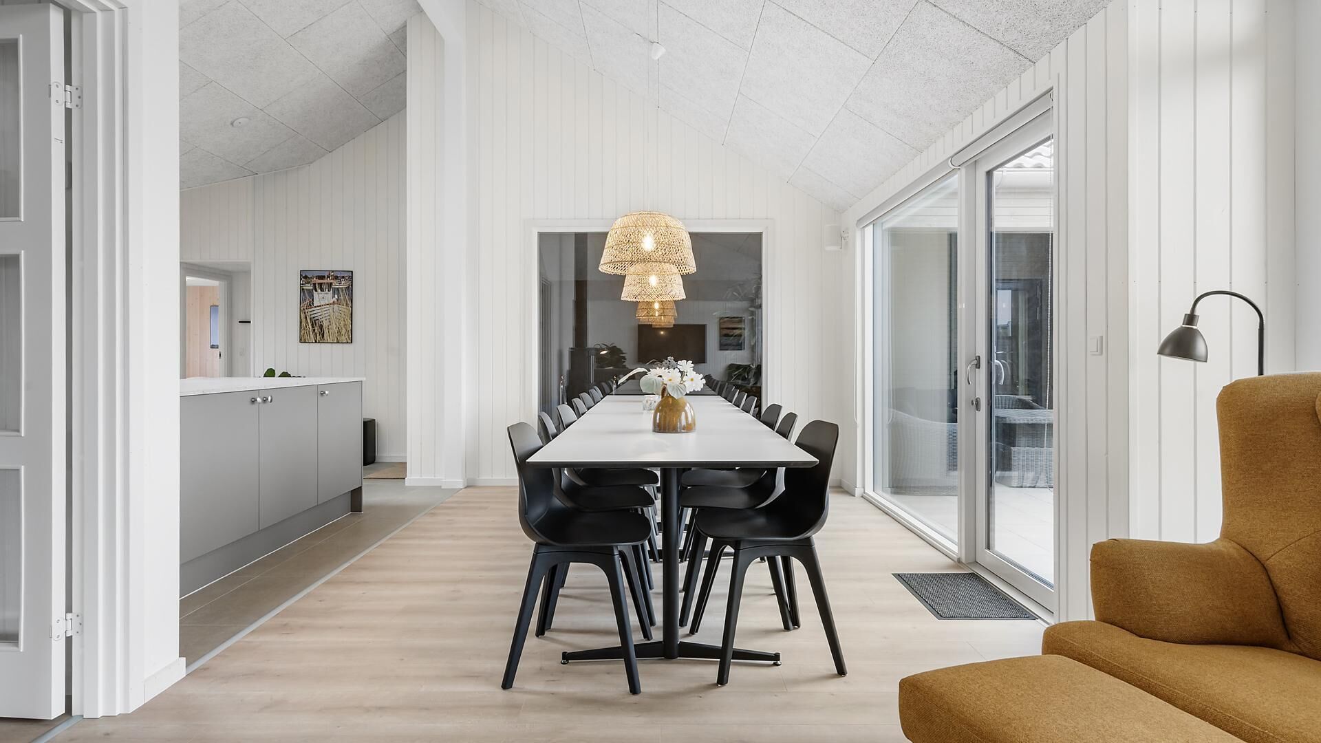A modern dining area with a long table, black chairs, and a central hanging light fixture.