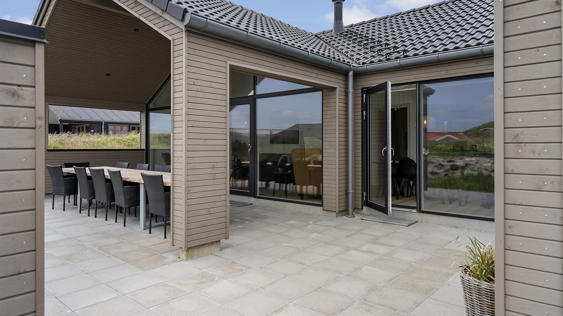 An outdoor patio area with a dining table and chairs, a covered seating area, and a glass door entrance.