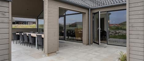 An outdoor patio area with a dining table and chairs, a covered seating area, and a glass door entrance.