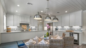 A modern kitchen with white cabinetry, a central island with seating, and pendant lighting. - A Perfect Day: Gulf Front! Rooftop Deck, Putt Putt, Pool Spa by Anna Maria Life (Anna Maria)