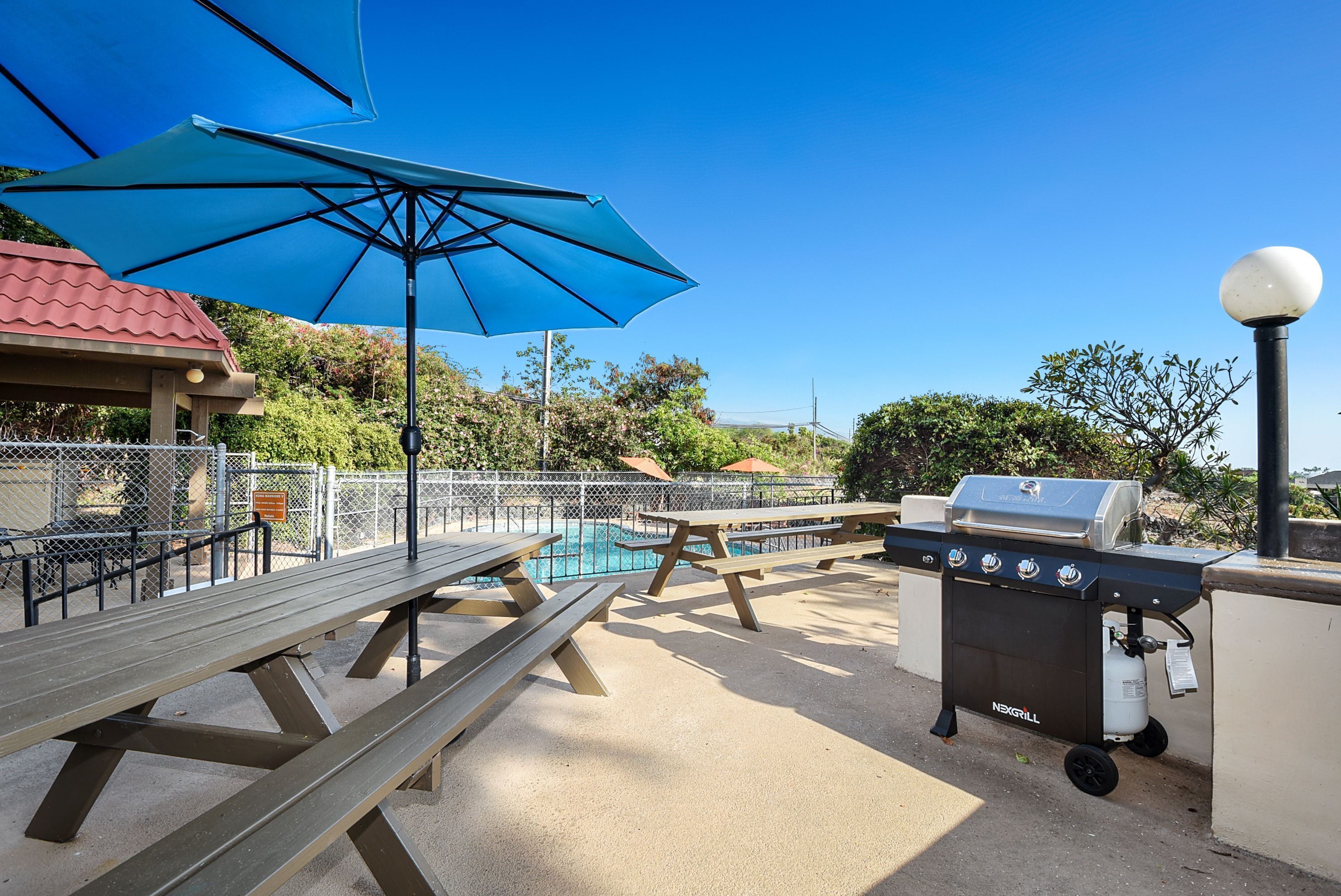 Un espace barbecue équipé d’un gril, de tables de pique-nique et d’une piscine.