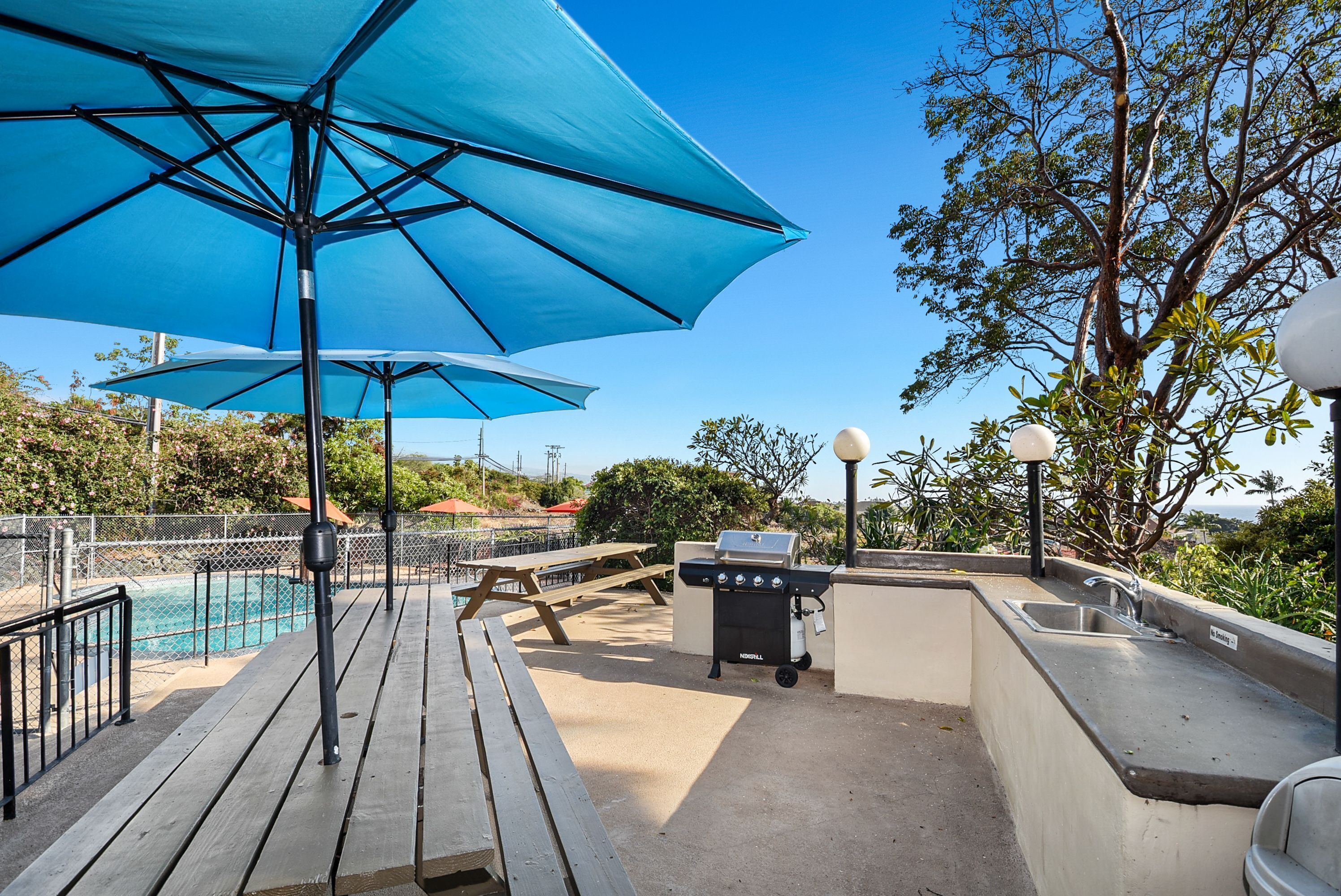 Um deck com churrasqueira, mesas de piquenique e piscina.