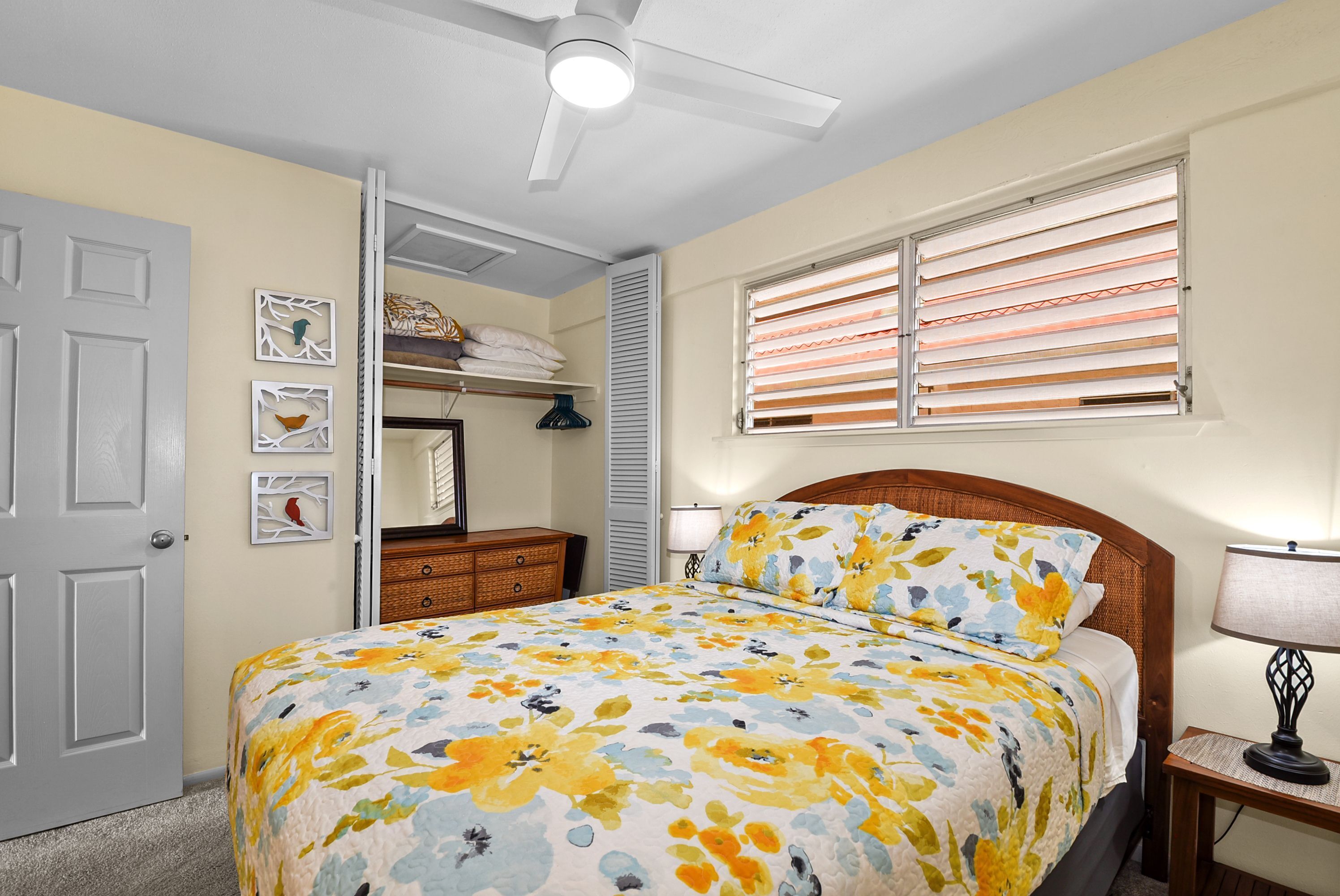A bedroom with a bed, a ceiling fan, a window with blinds, a bedside lamp, and a closet with shelves.