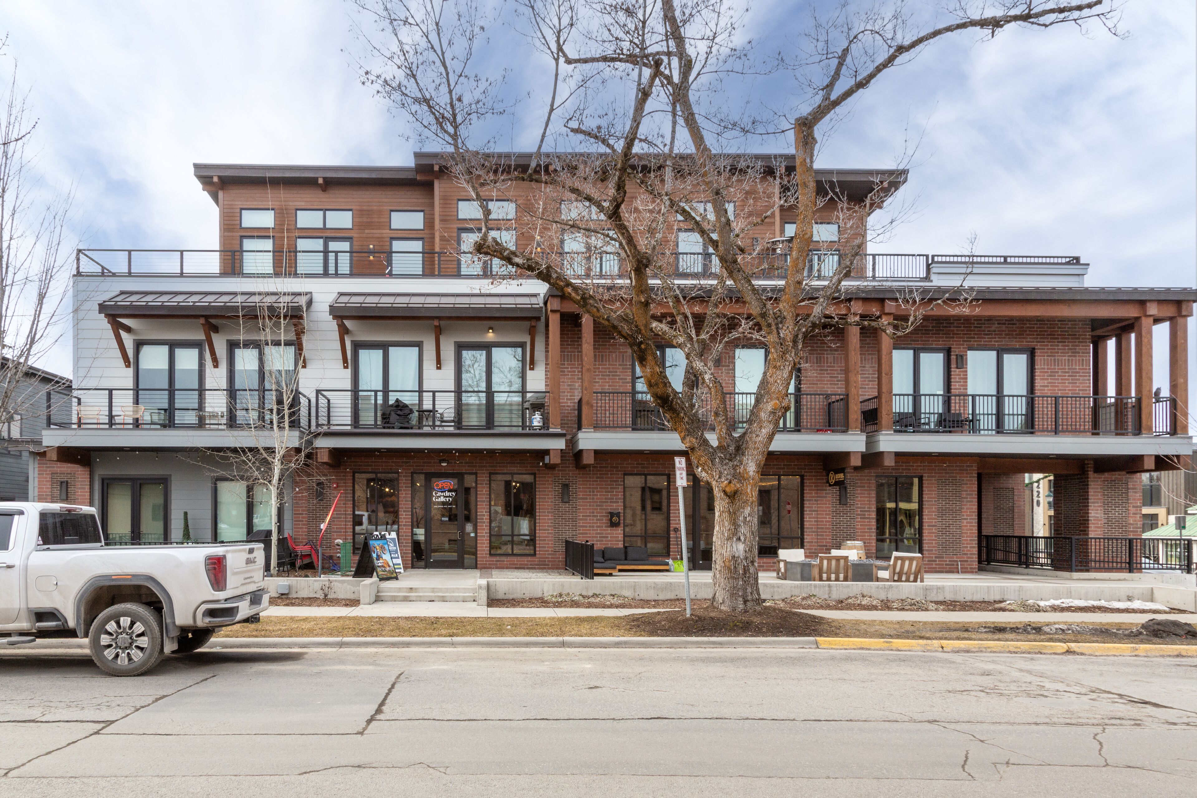 A multi-story building with a brick facade, large windows, and a tree in front.