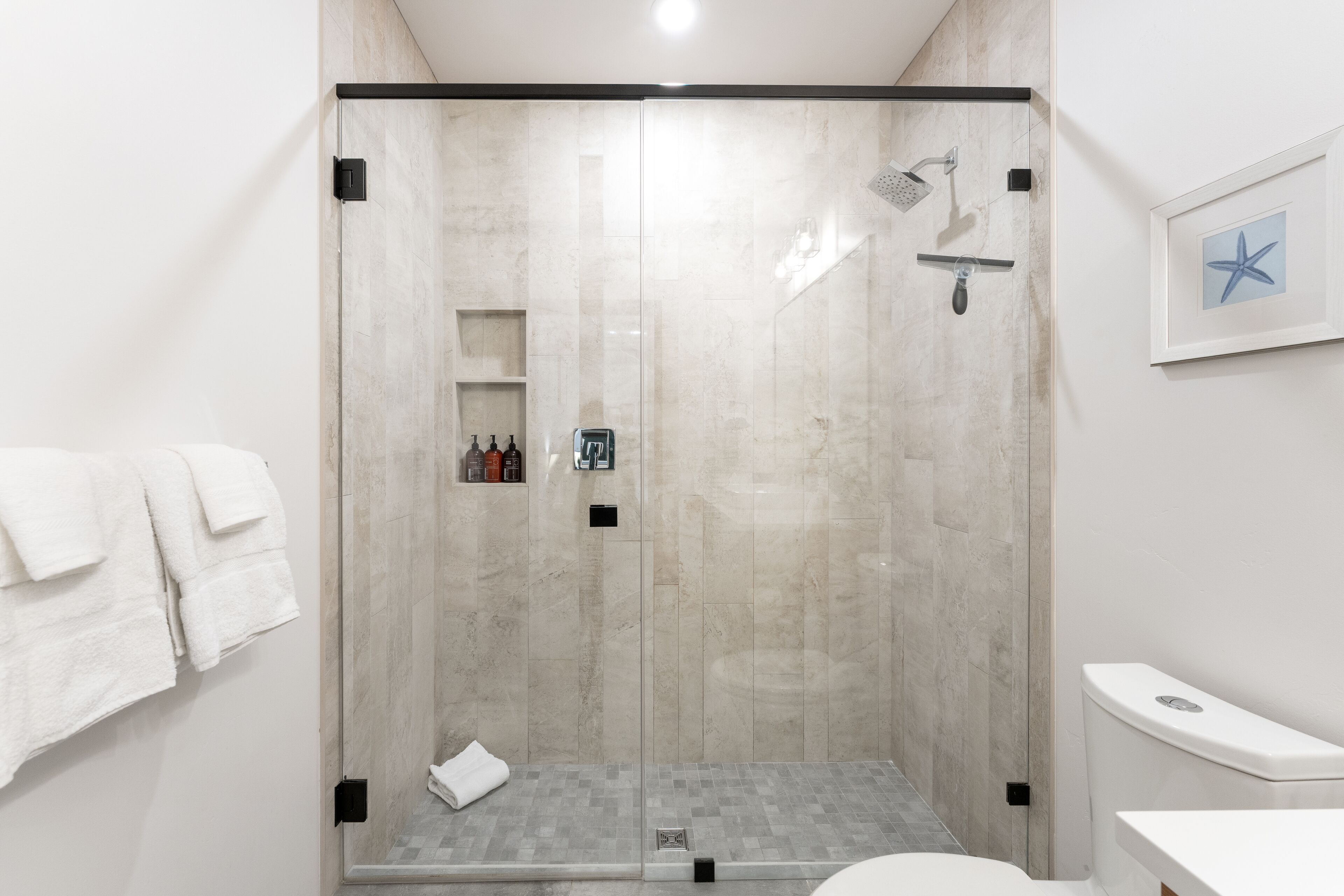 Une salle de bain moderne dotée d’une douche à parois de verre, de toilettes et d’un lavabo.