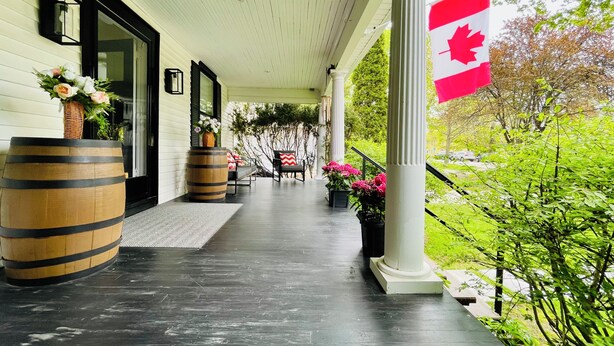 A covered porch with a Canadian flag, wooden barrels, outdoor seating, and potted plants. - King’s Gate
Fall Special • Old Town • 6 Parking • 4 King Beds (Niagara-on-the-Lake)