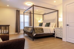 Un lit à baldaquin avec une table de chevet et une lampe, une chaise en bois et une fenêtre avec des rideaux.