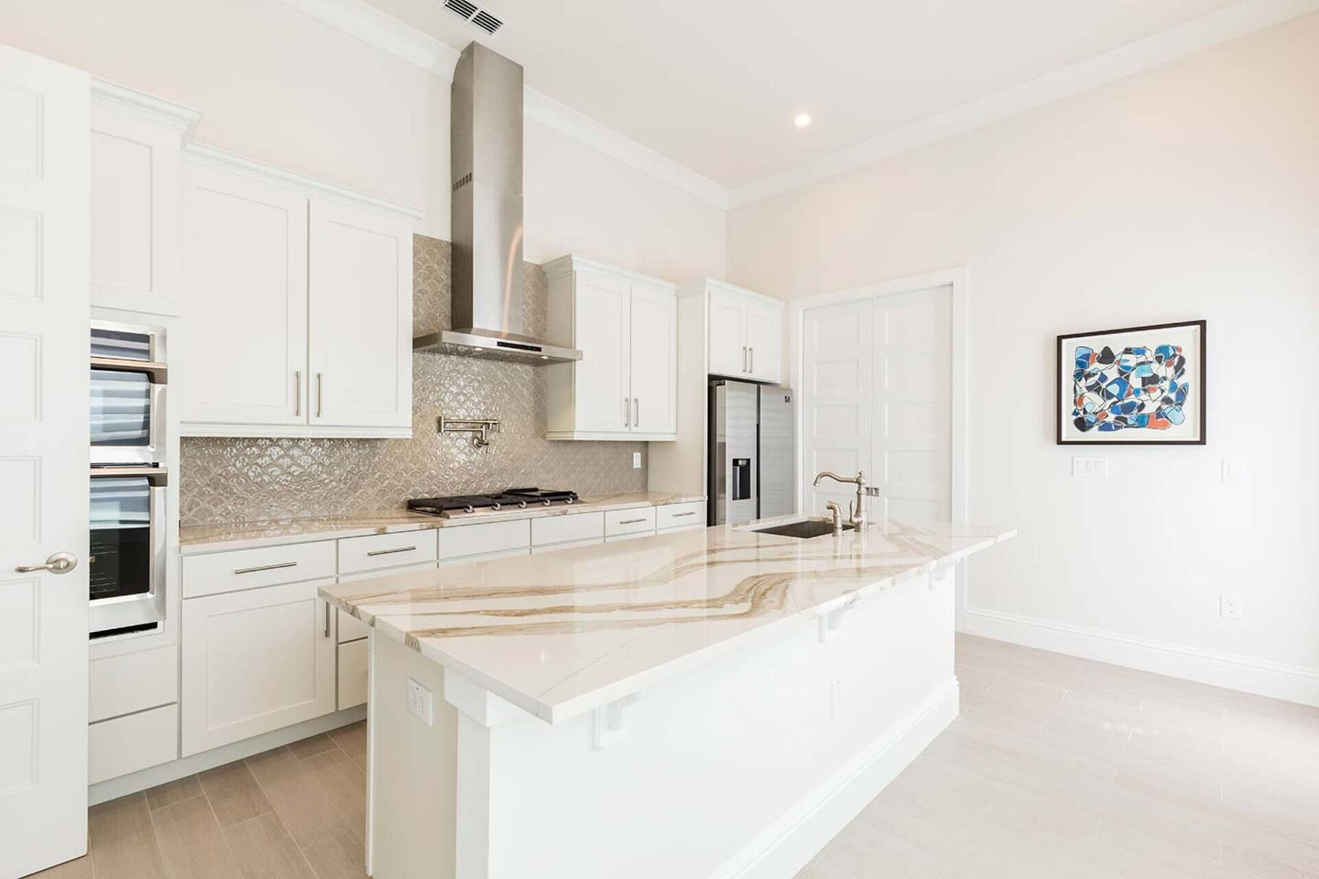 A modern kitchen with white cabinetry, a large island, and a stainless steel range hood.