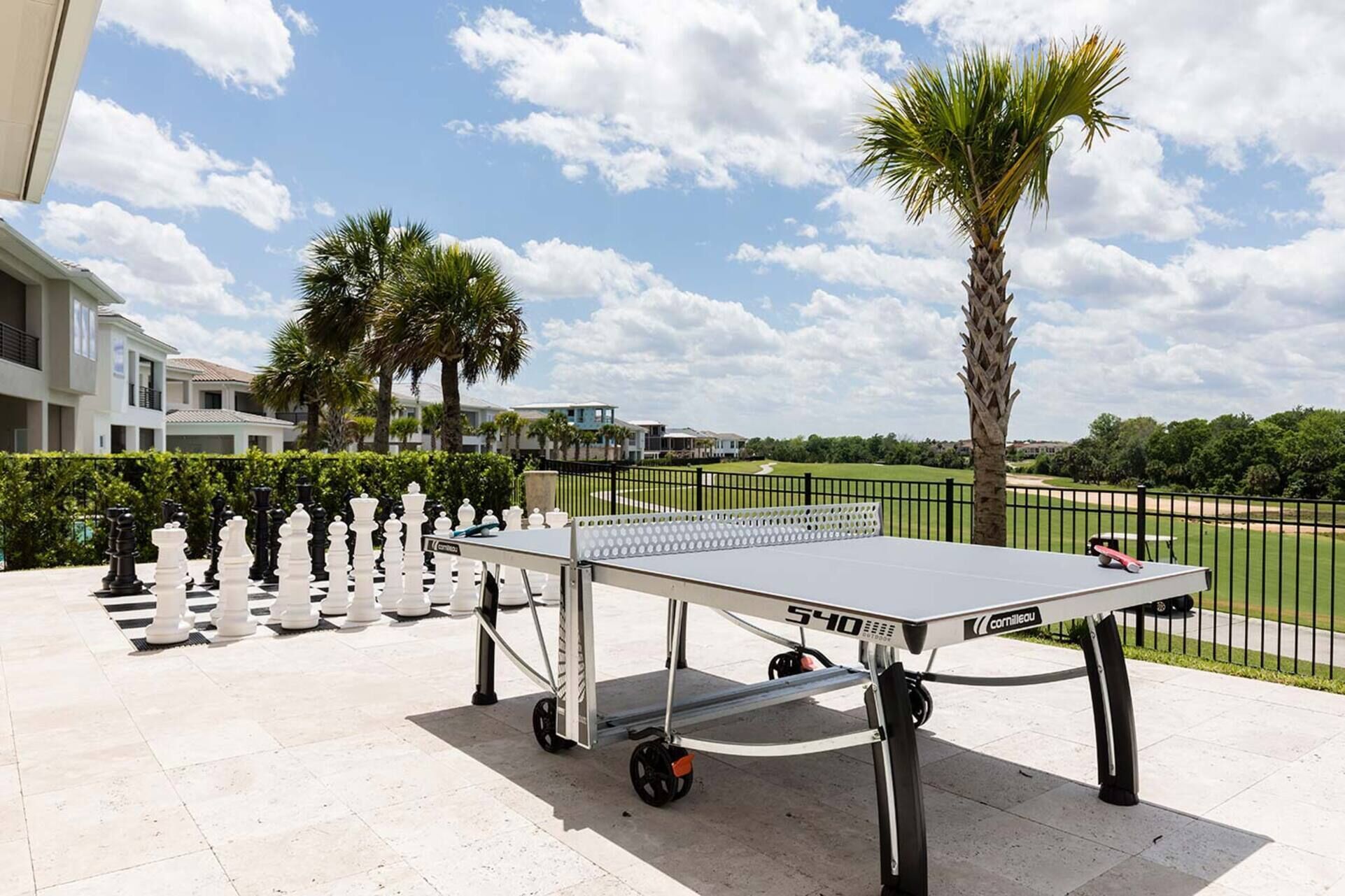 Une table de ping-pong portable installée en plein air, avec un ciel dégagé, des palmiers et un terrain de golf en arrière-plan.