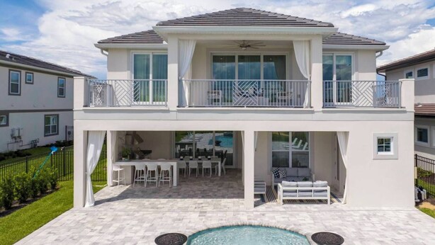 Una casa a due piani con un balcone, un patio con mobili da esterno e una piscina.