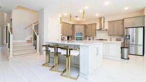 Una cucina moderna con un'isola centrale, elettrodomestici in acciaio inossidabile e una scala che conduce a un altro piano.