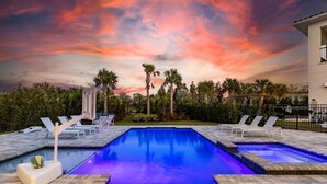 A swimming pool with two sides of lounge chairs, surrounded by palm trees and a building. - 5 Star Villa Aurelius – A Golden Grand Residence (Orlando)