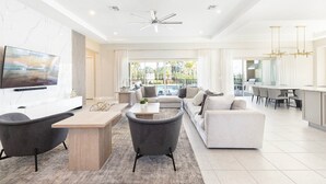 A spacious living area with a large TV, a dining table, and a sofa. - 5 Star Villa Aurelius – A Golden Grand Residence (Orlando)
