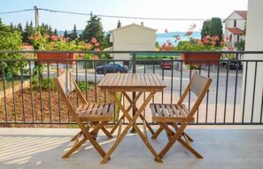 A balcony with a wooden table and two chairs, overlooking a street with parked cars and a building with a red roof. - Holiday apartment with balcony and air conditioning (Sv. Filip i Jakov)