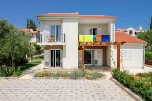 Ein zweistöckiges Haus mit gefliester Terrasse, Balkon und kleinem Garten.