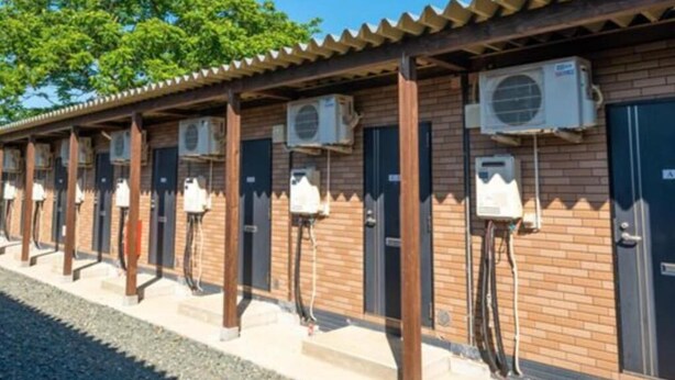 Une rangée de toilettes publiques extérieures, chacune équipée de sa propre unité de climatisation et dotée d’une façade en briques.