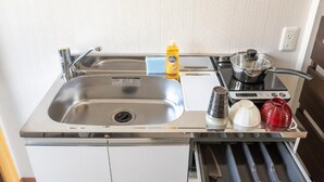 Une petite cuisine équipée avec un évier en acier inoxydable, une petite cuisinière et un tiroir intégré contenant des ustensiles.