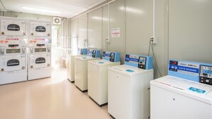 Une laverie équipée de plusieurs machines à laver et de plusieurs séchoirs, avec un panneau indiquant la capacité de charge et une affiche de consignes de sécurité sur le mur.