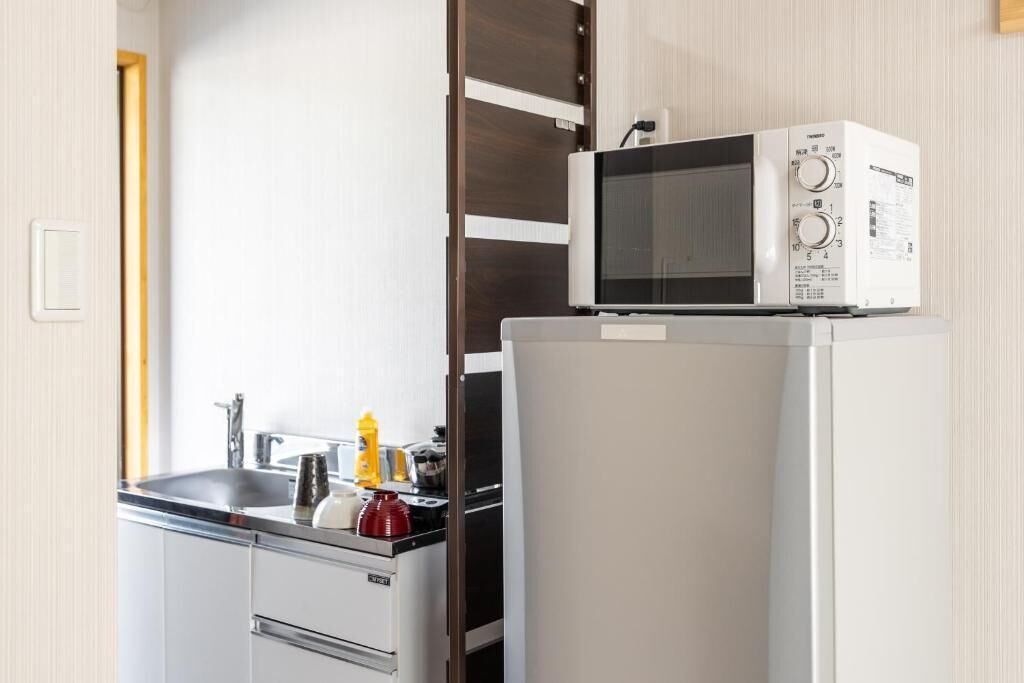 A compact kitchen with a microwave on top of a refrigerator, a sink, and a countertop with various kitchen items.