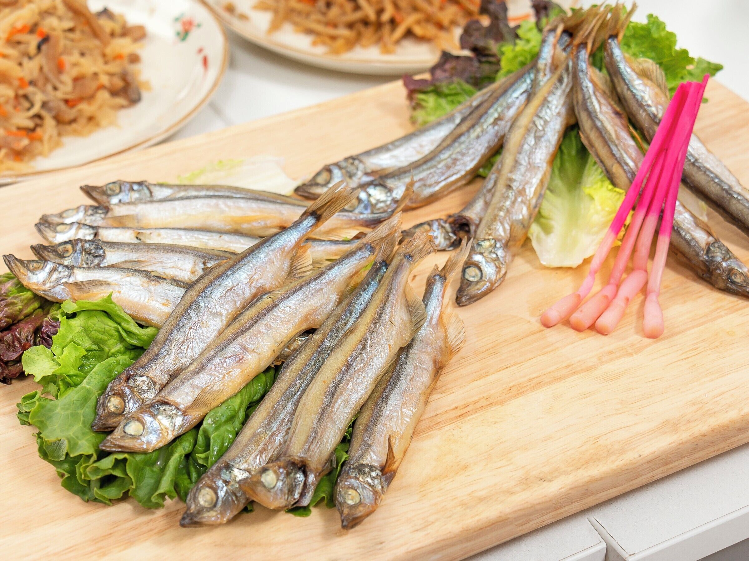 Una tabla de madera con pescado seco, lechuga y verduras rosadas encurtidas.