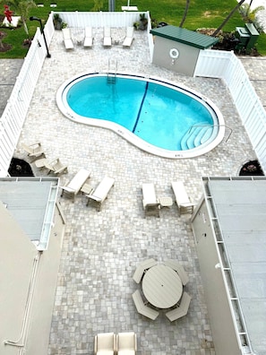 Ein Swimmingpool mit gefliestem Sonnendeck, Liegestühlen und einem Tisch.