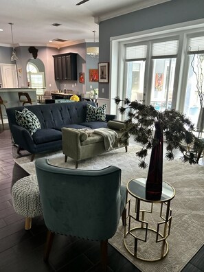 Ein modernes Wohnzimmer mit einer Couch, Sesseln und einem Couchtisch. Im Hintergrund ist ein Essbereich mit einer sichtbaren Küche zu sehen.