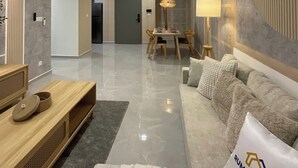 A modern living room with a sofa, a coffee table, and a dining area with chairs. There is a ceiling fan, a lamp, and an air conditioning unit. - Earthy 2BR @ Agile BB | Wi-Fi + Netflix (Kuala Lumpur)