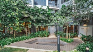 A courtyard with a central seating area, surrounded by lush greenery and a building with multiple floors. - Earthy 2BR @ Agile BB | Wi-Fi + Netflix (Kuala Lumpur)