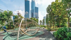 A playground with a rope climbing structure, surrounded by greenery and modern buildings in the background. - Earthy 2BR @ Agile BB | Wi-Fi + Netflix (Kuala Lumpur)