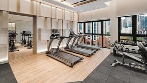 A modern gym with treadmills, weight machines, and a large window offering a city view. - Earthy 2BR @ Agile BB | Wi-Fi + Netflix (Kuala Lumpur)