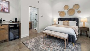 A bedroom with a large bed, bedside lamps, a bench, a rug, and a wall with decorative plates. - Goldstone Casita 6 at Featherstone Ranch Vineyards (Stonewall)