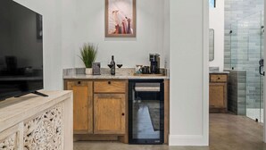 A modern kitchen with a built-in dishwasher, wooden cabinets, a flat-screen TV, and a framed artwork above the counter. - Goldstone Casita 6 at Featherstone Ranch Vineyards (Stonewall)
