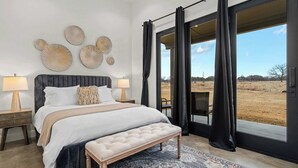 A bedroom with a large bed, a bench, a nightstand, and a view of the outdoors through a sliding door. - Goldstone Casita 6 at Featherstone Ranch Vineyards (Stonewall)