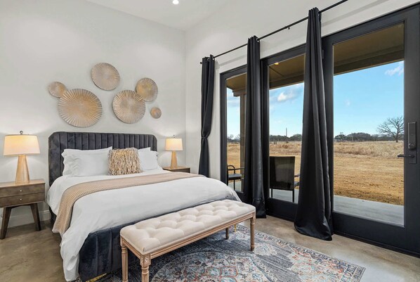 A bedroom with a large bed, a bench, a nightstand, and a view of the outdoors through a sliding door. - Goldstone Casita 6 at Featherstone Ranch Vineyards (Stonewall)