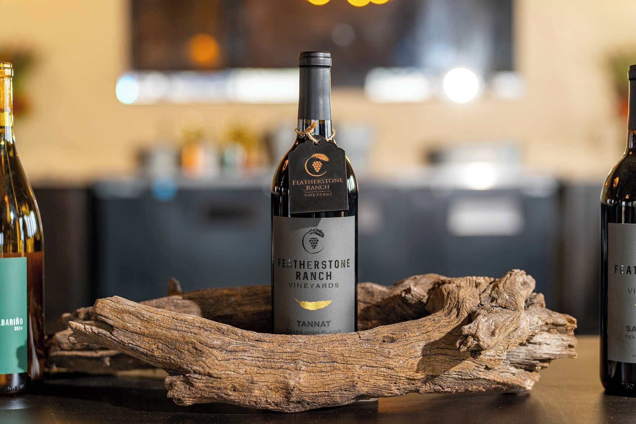 A bottle of Featherstone Ranch Tannat wine on a wooden surface with a blurred background.