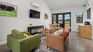 Ein modernes Wohnzimmer mit einem grünen Sofa, einem braunen Sofa, einem Couchtisch und einem an der Wand befestigten Fernseher. Es gibt einen Essbereich mit Tisch und Stühlen sowie eine Küchenzeile mit Arbeitsplatte und Schränken.