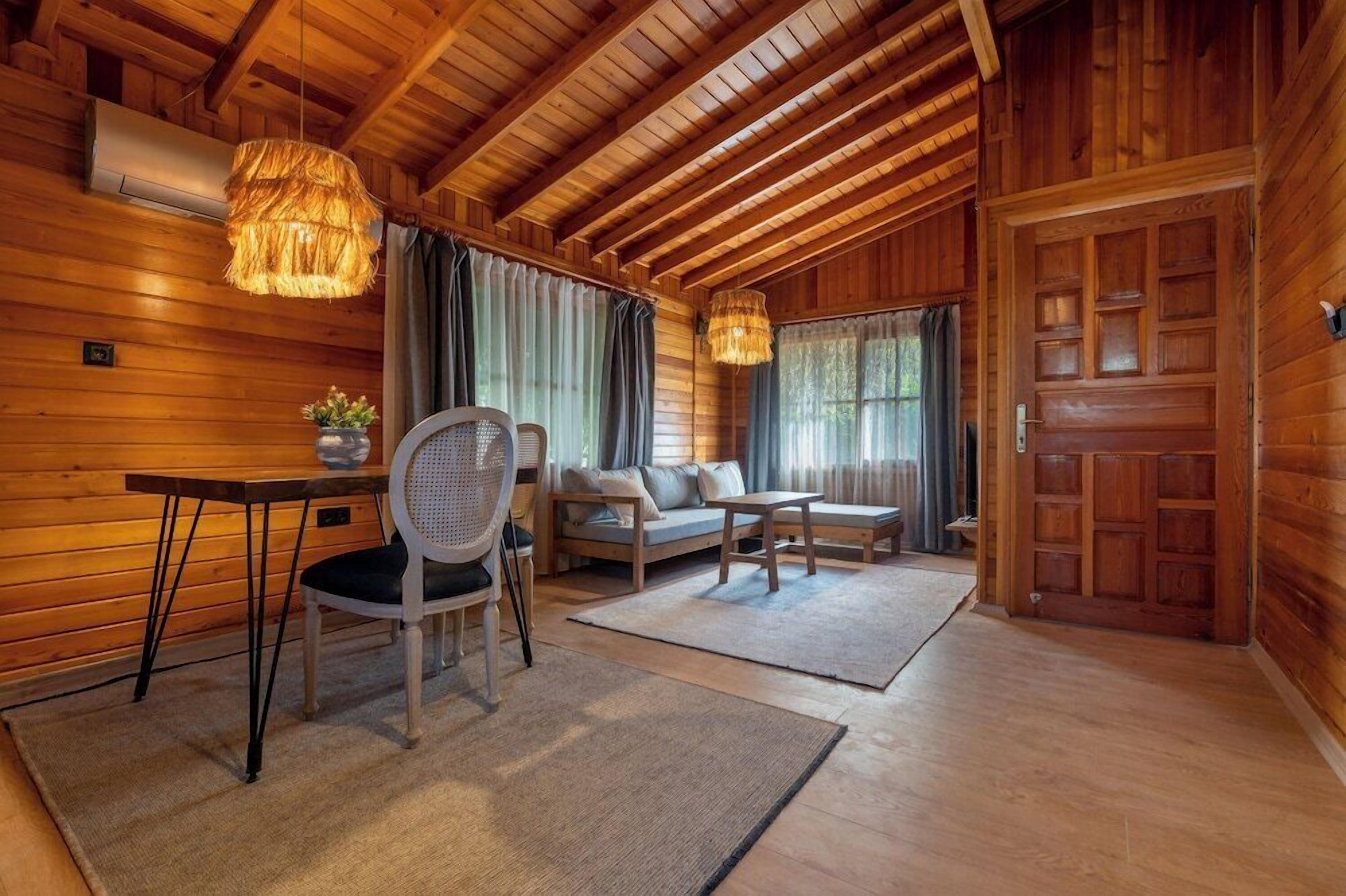 A cozy wooden cabin interior with a dining table, chairs, a sofa, and a large wooden door.