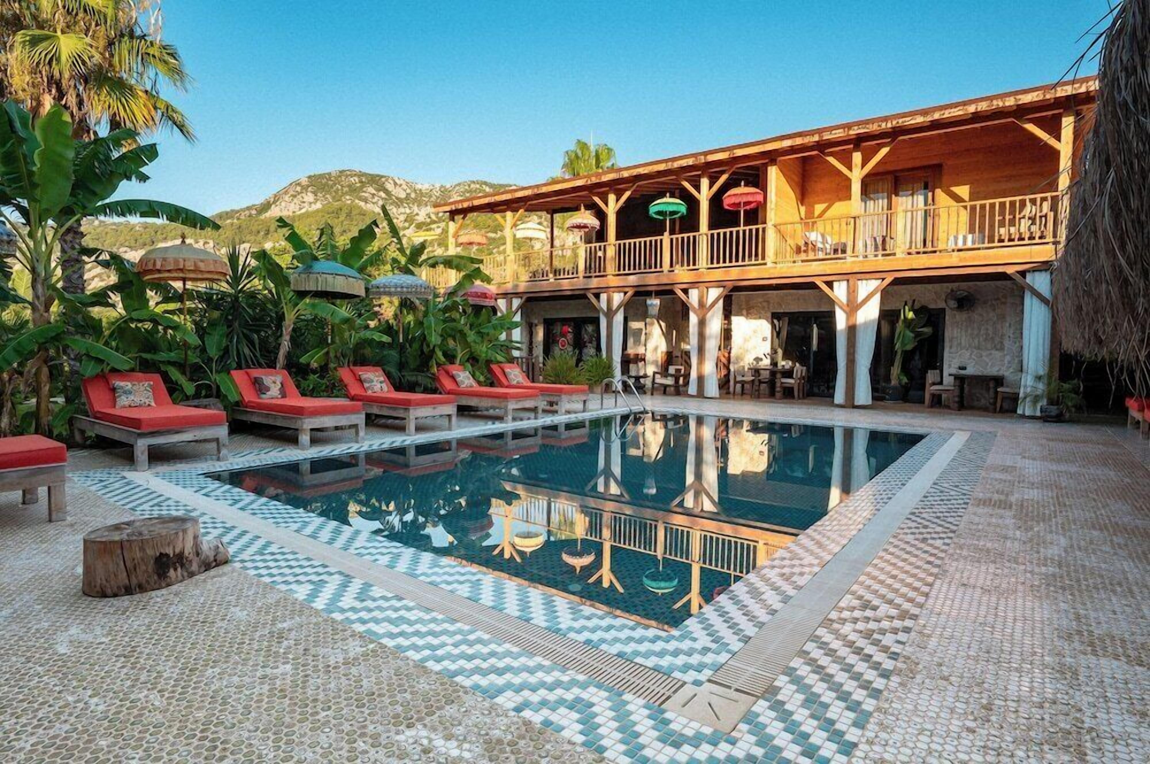A pool area with lounge chairs, a wooden deck, and a building with a balcony.
