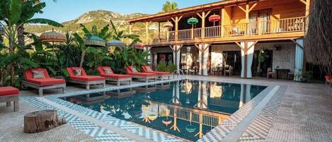 A pool area with lounge chairs, a wooden deck, and a building with a balcony.