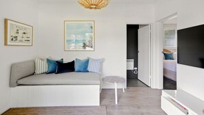 A modern living room with a grey sofa, blue and white cushions, a small round table, and a large TV on a white stand. - NEW! The Soak House- Walk to the beach! (Lorne)