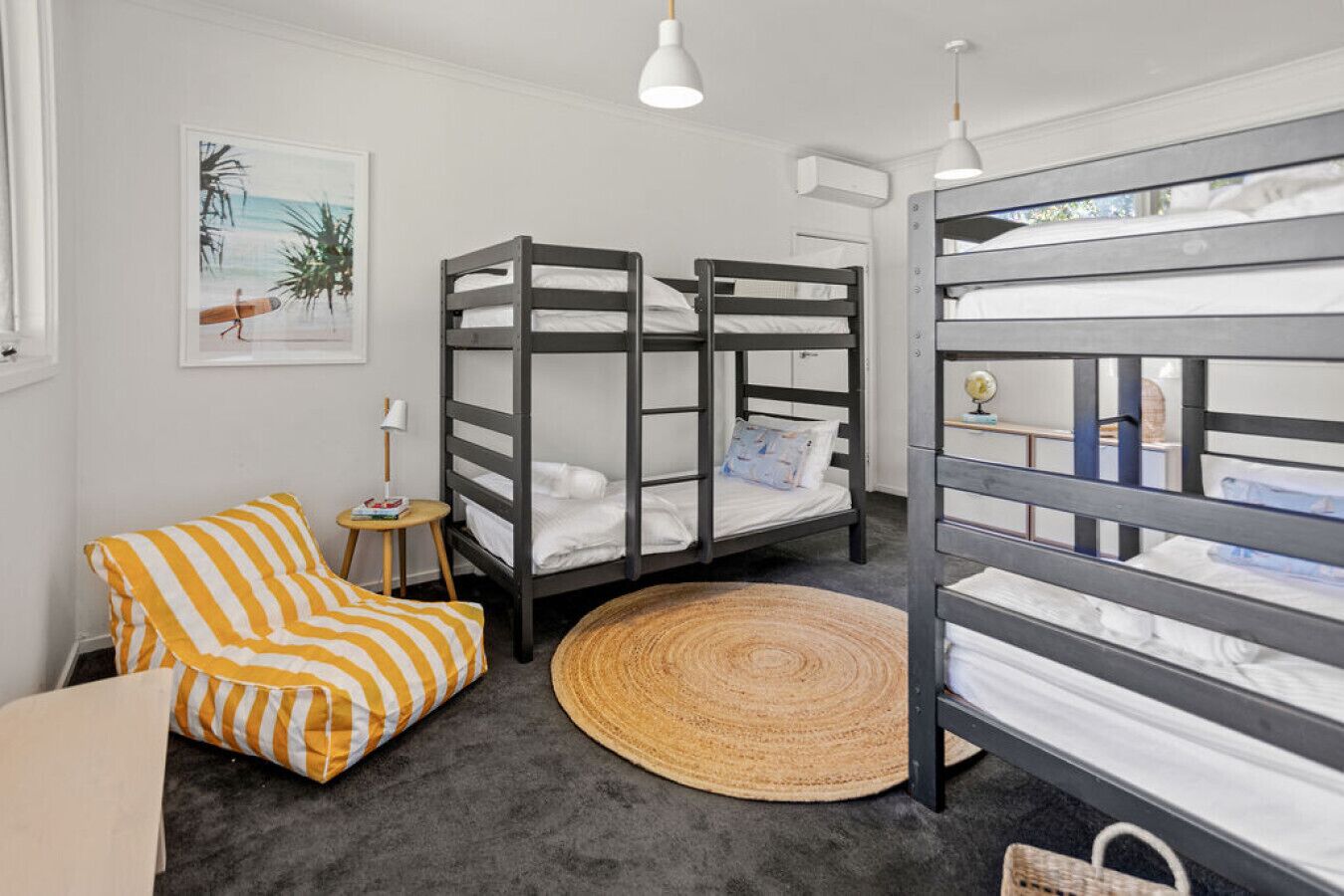 A room with bunk beds, a striped chair, a small table, and a woven rug.