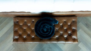 Een bruine sofa met tufting en een opgerolde, donkergekleurde deken of vloerkleed.