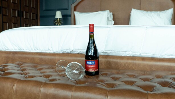 Een bed met een fles wijn en een glas op een gestoffeerd hoofdeinde.