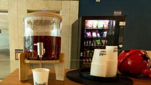 Een drankdispenser, een stapel wegwerpbekers en een automaat in een commerciële omgeving.