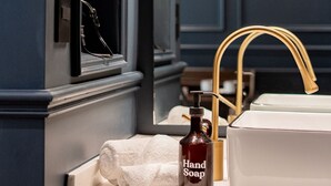Een badkamer met een donkerblauwe wand, een wit wastafelmeubel met een gouden kraan, een handzeepfles en een handdoek.