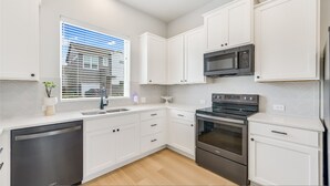 A modern kitchen with white cabinets, a built-in microwave, a stainless steel oven, and a dishwasher. - Spacious 2BR Flex Room Home Near Tech Campuses (Pflugerville)