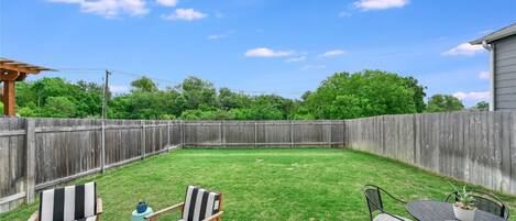 A backyard with a wooden fence, a concrete patio, and outdoor furniture including two striped chairs and a table.