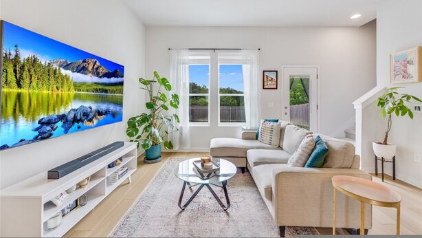 A modern living room with a large flat-screen TV, a sofa, a coffee table, and potted plants. - Spacious 2BR Flex Room Home Near Tech Campuses (Pflugerville)